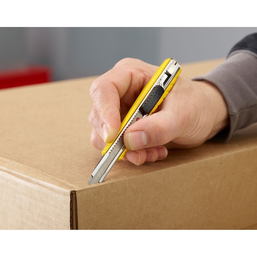 STANLEY 0-10-411 yellow utility knife cutting cardboard box, close-up in use.