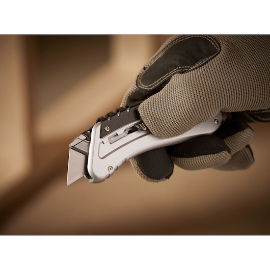 STANLEY 0-10-810 folding utility knife held in gloved hand, showing metallic body and exposed blade.