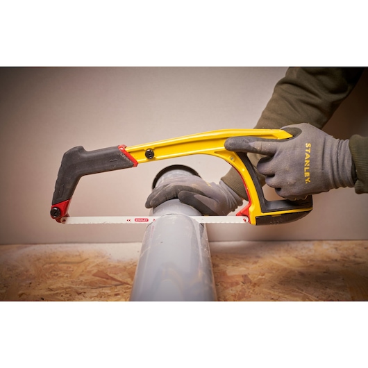 Photo of STANLEY 0-20-108 hacksaw cutting a grey pipe, user wearing grey gloves.