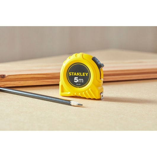 STANLEY 0-30-497 yellow 5m tape measure on a workbench with a pencil and piece of wood in the background.