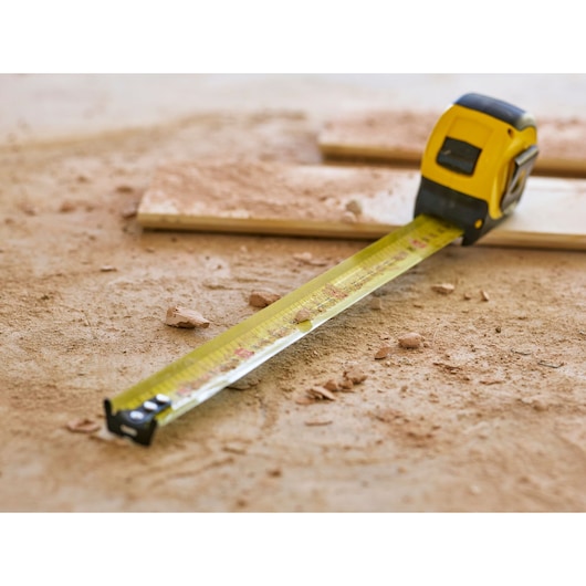 STANLEY 0-33-728 tape measure on a dusty workshop floor, extended and surrounded by wood and debris.
