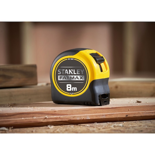 STANLEY 0-33-728 tape measure FATMAX 8m, yellow and black, side view, on wooden surface.