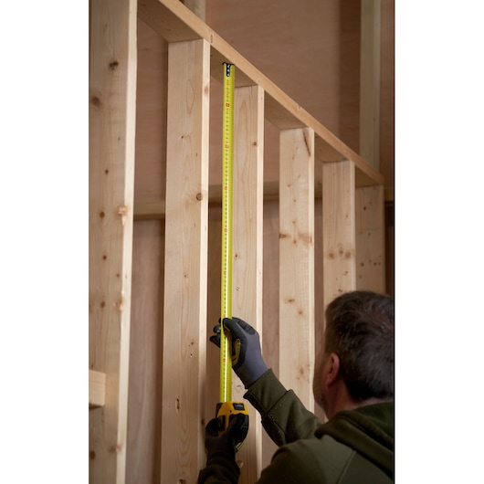 STANLEY 0-33-811 tape measure measuring vertical wooden stud in construction setting.