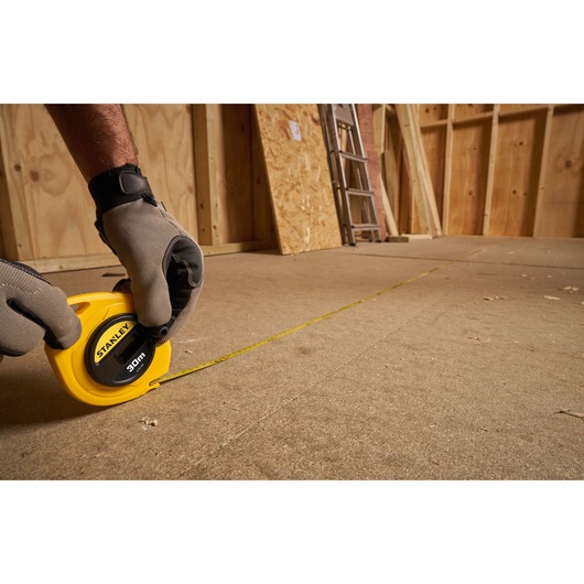 STANLEY 0-34-108 measuring tape, yellow, used on construction floor, person wearing gloves.