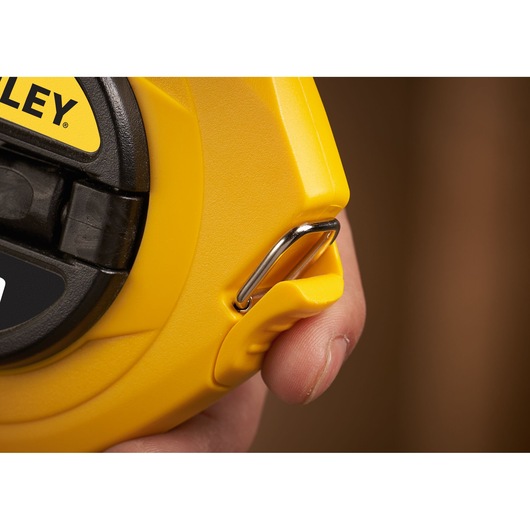 STANLEY 0-34-108 tape measure close-up showing yellow case, metal hook, and part of hand holding it.