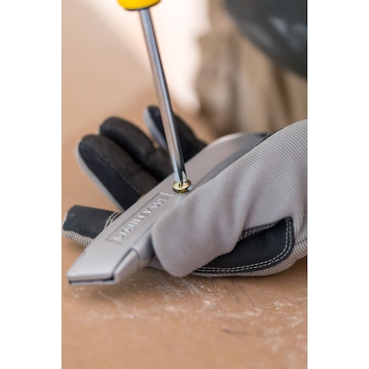 Photo of a STANLEY 1-10-099 utility knife being tightened with a screwdriver, held by a gloved hand.