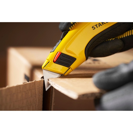Stanley 1-11-700 utility knife cutting cardboard, close-up photography with glove holding tool.
