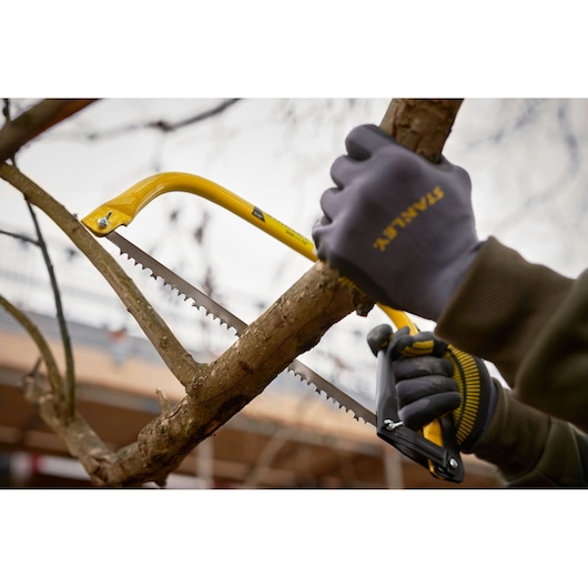 STANLEY 1-20-447 hand saw cutting tree branch with gloved hands, yellow frame, close-up outdoor photo.