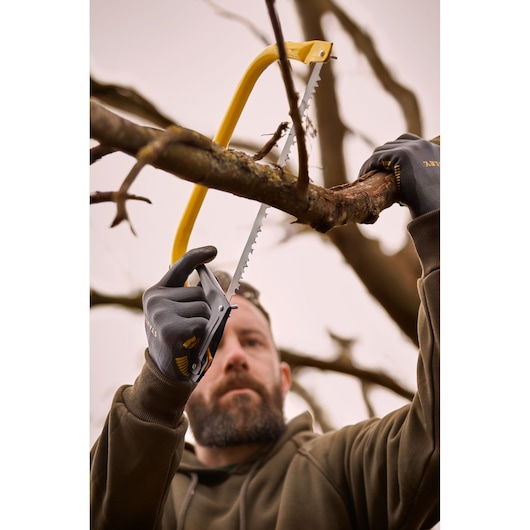 STANLEY 1-20-447 hand saw cutting a tree branch outdoors, person wearing gloves.