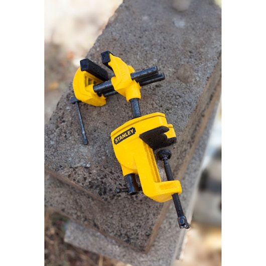 STANLEY 1-83-069 yellow bench vise clamp on concrete block, photography product view.