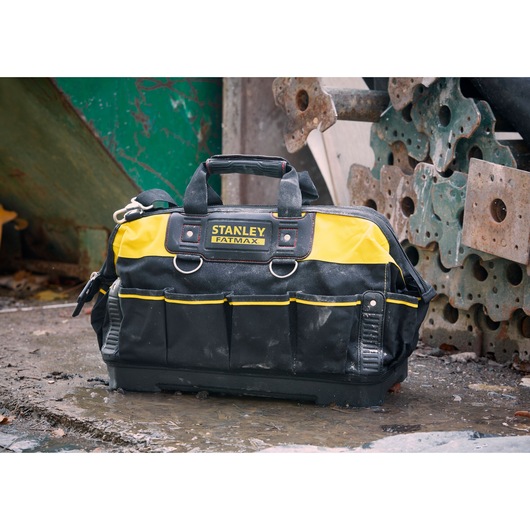STANLEY 1-93-950 tool bag with yellow and black fabric, multiple pockets, handles, shown outdoors on wet ground.