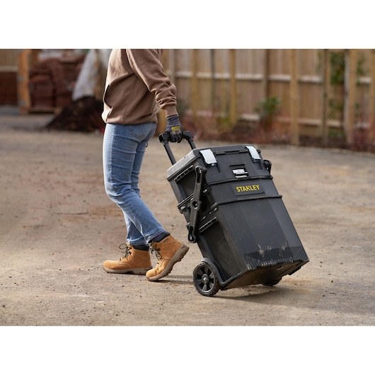 STANLEY 1-94-210 rolling toolbox being pulled outdoors by a person wearing jeans and work boots.