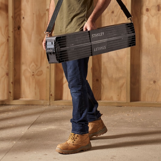 STANLEY 1-97-475 portable black folding sawhorse with shoulder strap, shown being carried on jobsite.