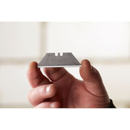 STANLEY 2-11-700 utility blade held between fingers, close-up view, silver color, sharp edge visible.