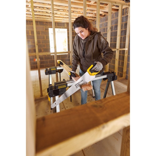 Photo of STANLEY 2-15-244 hand saw in use, cutting wood on sawhorse at construction site.
