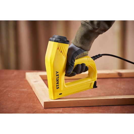 STANLEY 6-TRE550 electric stapler in use on wood frame, yellow body, close-up side angle.