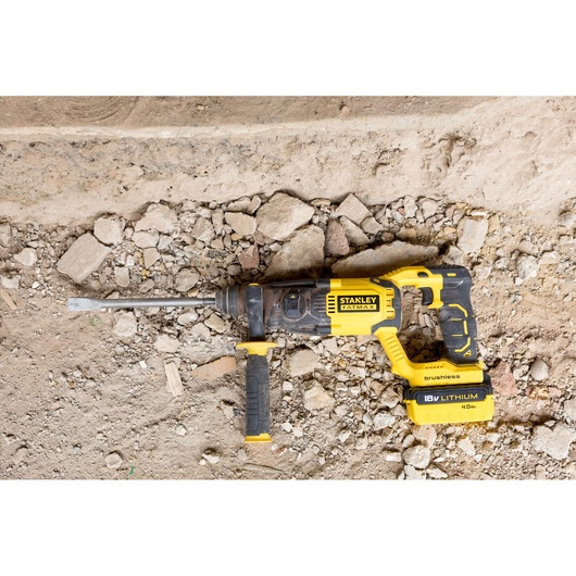STANLEY FMCD900B rotary hammer drill, yellow and black, photographed on rocky construction ground.