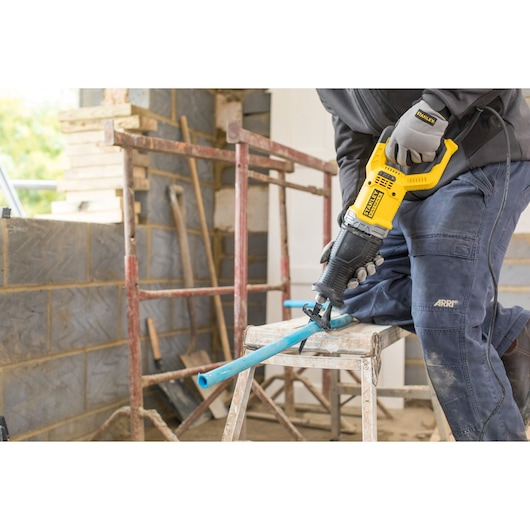 STANLEY FME360 reciprocating saw in use cutting a blue pipe at a construction site, angled side view.