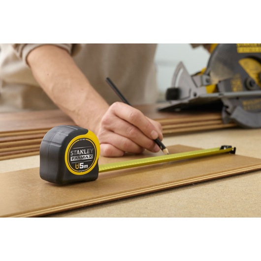 STANLEY FMHT0-33864 tape measure used for marking wood, yellow and black casing, close-up photography.