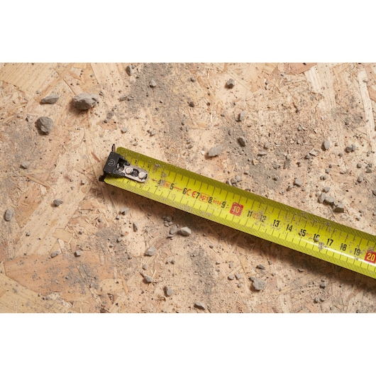 STANLEY FMHT0-33864 yellow tape measure on dusty plywood surface with scattered debris.