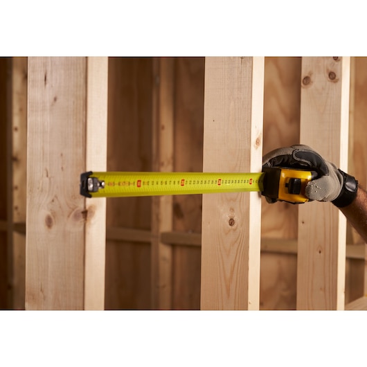 STANLEY FMHT0-33868 tape measure being used to measure wooden studs, close-up, construction setting.
