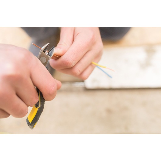 STANLEY FMHT0-80518 diagonal pliers held cutting colored electrical wires, close-up photo.