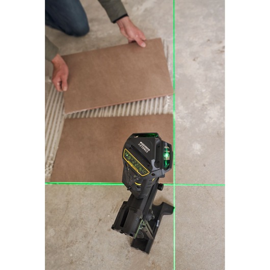 STANLEY FMHT1-77356 laser level on stand projecting green lines for tile alignment, photography view from above.