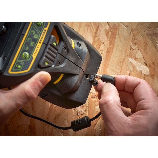 STANLEY FMHT1-77356 photography showing hands plugging power cable into black and yellow device on wood surface.