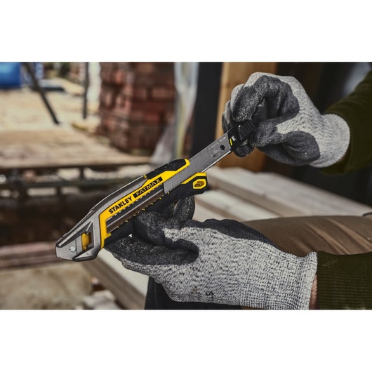 Photo of STANLEY FMHT10594-0 utility knife held by gloved hands at a construction site.