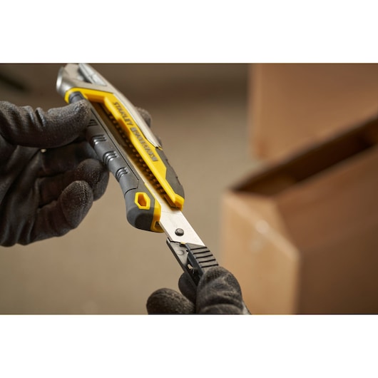 STANLEY FMHT10594-0 utility knife with yellow and black grip, close-up in gloved hands, workspace background.