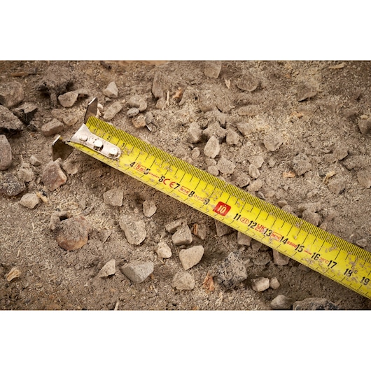 STANLEY FMHT38214-0 tape measure with yellow blade on rocky ground, close-up photography.