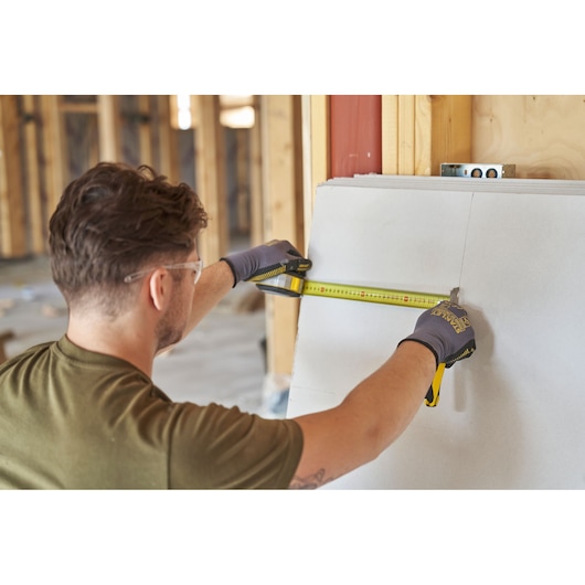 Photo of STANLEY FMHT38217-0 tape measure in use, person measuring drywall in construction setting.