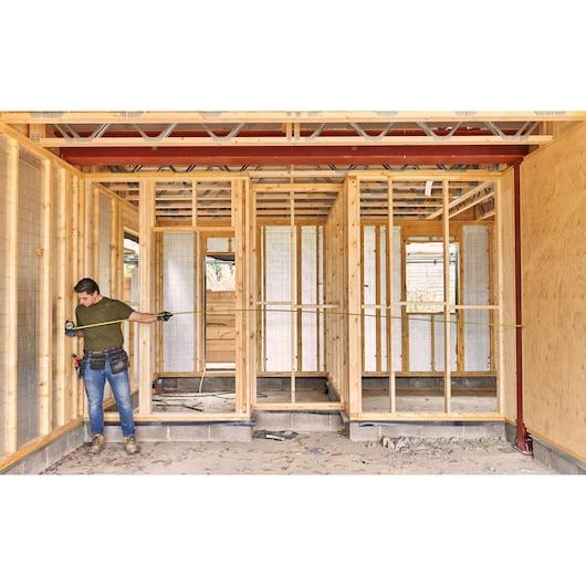 STANLEY FMHT38232-0 tape measure used by worker measuring wooden frame in building under construction.
