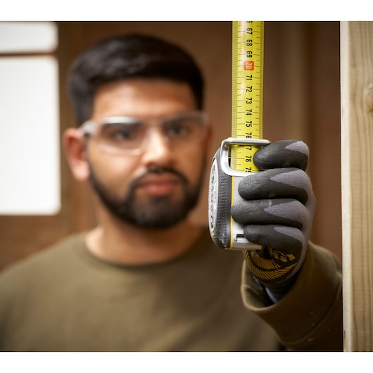 Photo of STANLEY FMHT38232-0 tape measure in a gloved hand measuring wood, close-up view.