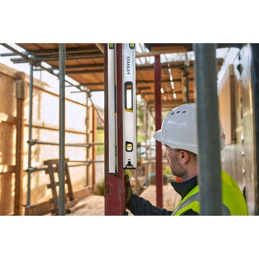 STANLEY FMHT43677 spirit level used by a worker in a construction site, close-up side angle.