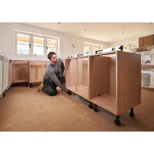 Photo of STANLEY FMHT43677 spirit level placed on wooden kitchen cabinet frame during installation, wide angle.