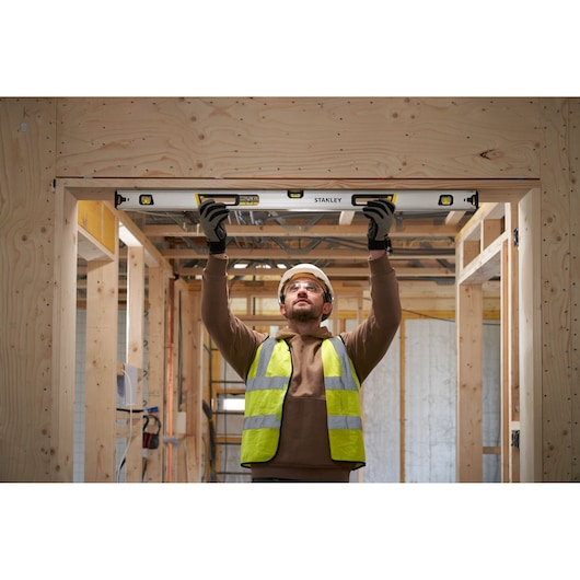 Photo of worker using STANLEY FMHT43677 spirit level in a wooden construction site, holding it above his head.