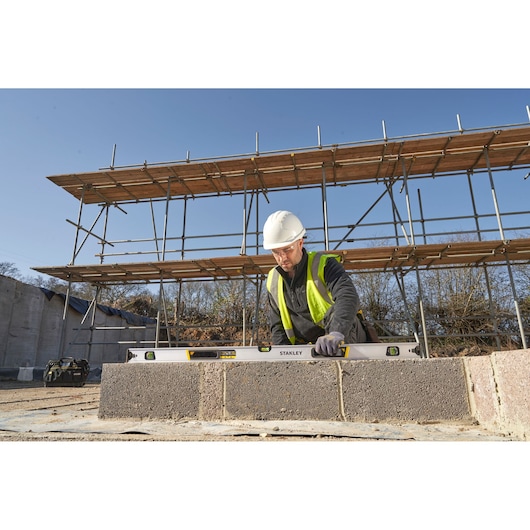 Photo of STANLEY FMHT43677 spirit level in use on a construction site, worker in safety gear measuring concrete blocks.