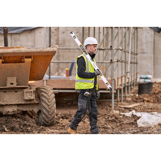 STANLEY FMHT43677 spirit level held by worker at construction site, full length side view.