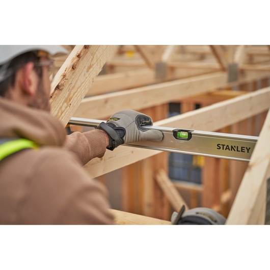 Stanley FMHT43679-1 level tool in use on wooden beams, worker wearing gloves and safety gear.