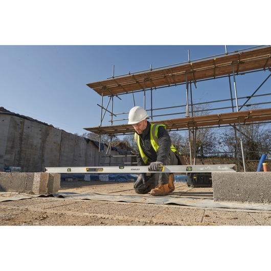 STANLEY FMHT43680-1 spirit level used by a construction worker kneeling at a building site, outdoor setting.
