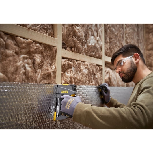 STANLEY FMHT6-70868 staple gun used on insulation by gloved worker, shown in construction setting.