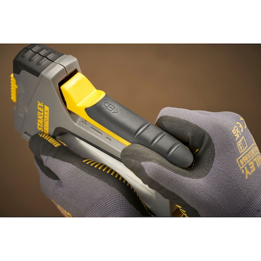 Photo of STANLEY FMHT6-70868 grey and yellow staple gun held by gloved hands, close-up angle.