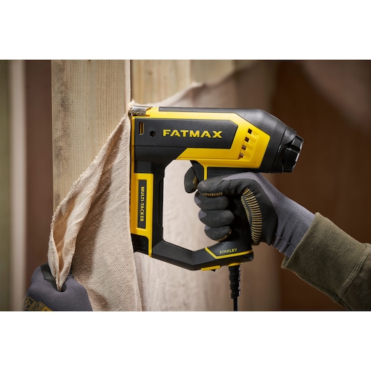 STANLEY FMHT6-75934 FATMAX multitacker stapler used to attach fabric to wooden frame, close-up.