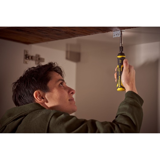 Person using STANLEY FMHT66719-0 ratcheting screwdriver under a wooden cabinet, yellow and black handle visible.