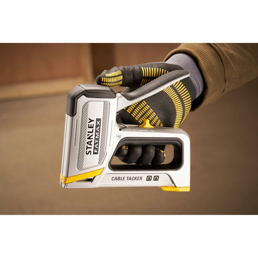 Stanley FMHT70100-0 cable tacker held in gloved hand, silver and yellow, side view.
