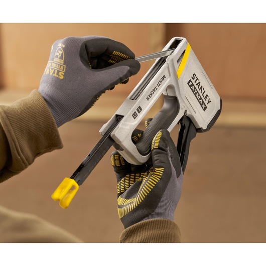 Photo of STANLEY FMHT70443-0 multi-tacker tool loaded with staples, held by gloved hands during use.