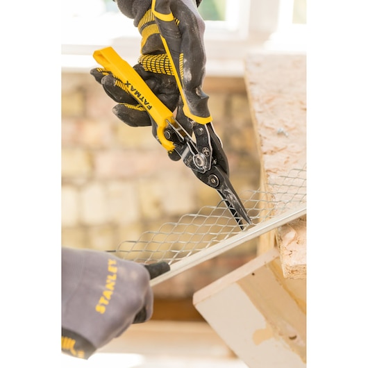 STANLEY FMHT73756-0 aviation snips cutting metal mesh, close-up, with gloved hands in a workshop.
