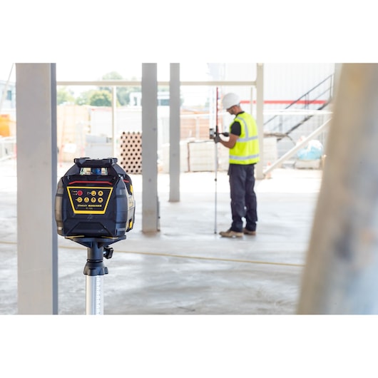 STANLEY FMHT77447-1 rotary laser level on tripod, construction site background, worker measuring.