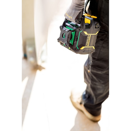 STANLEY FMHT77448-1 laser level held by a worker wearing black pants and gloves, outdoor setting.